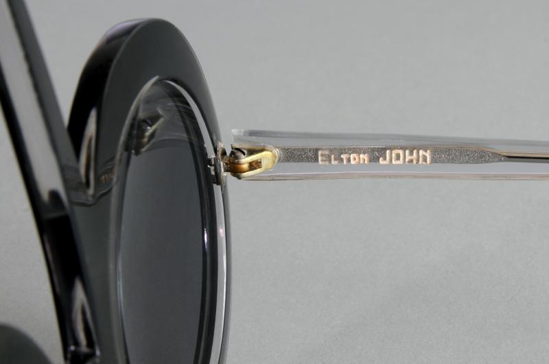 Paire de lunettes d’ELTON JOHN, en forme de notes de musique, en acétate teinté noir, les branches translucides en partie pailletées gris. L'intérieur de la branche droite gravé en lettres blanches : « Elton John ».