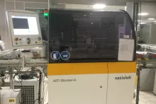 Machine de blocage et de déblocage sans alliage ART développée par Satisloh. La technologie remplace l’utilisation du métal fusible par de la colle UV et permet de s’affranchir du film de protection pour protéger la face avant du verre. Ce procédé de fabrication est moins polluant pour l’environnement