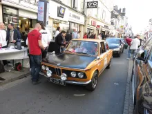 La BMW 2002 Tii pilotée par Philippe Roche est devant un point de contrôle d’un magasin Optic 2000