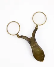 Lunettes chapeau, vermeil et cuir, XXe siècle. Pièce très rare qui s’accrochait au chapeau-melon par un petit crochet. ©Musée de la Lunette - coll. Essilor-Pierre Marly. Photo : Pierre Guénat